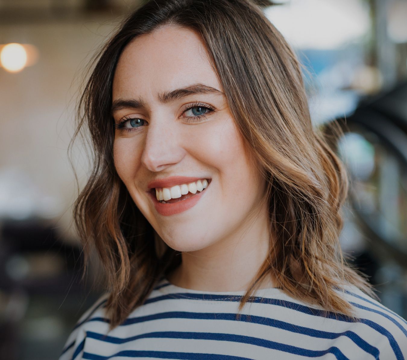 Smiling woman with wavy hair wearing striped shirt.